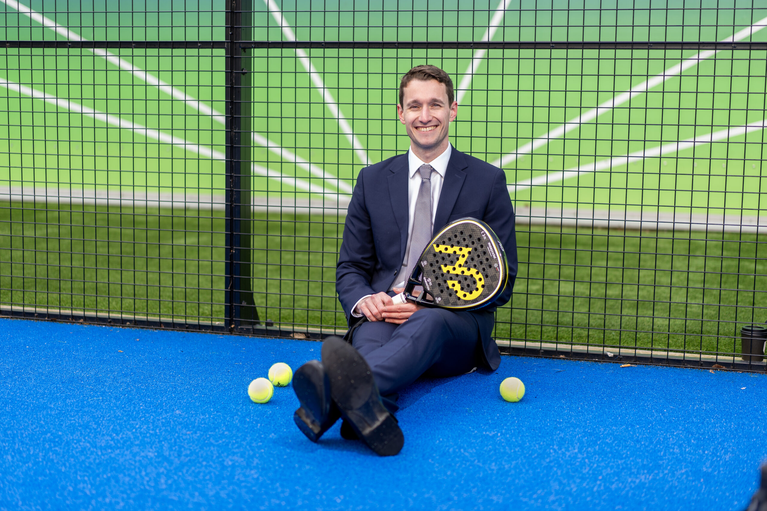 Max England sitting in a padel court in a suit