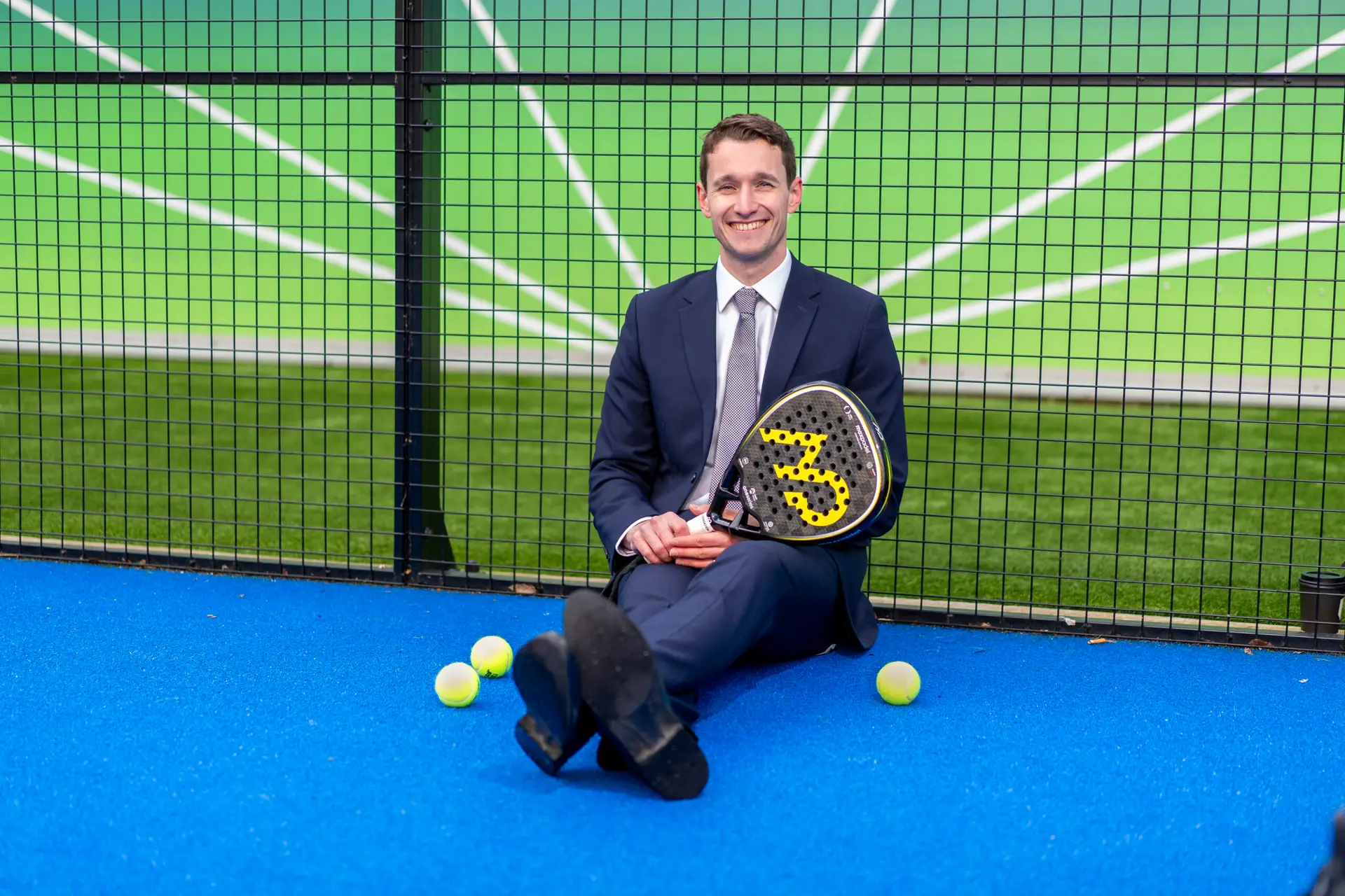 Max England sitting in a padel court in a suit