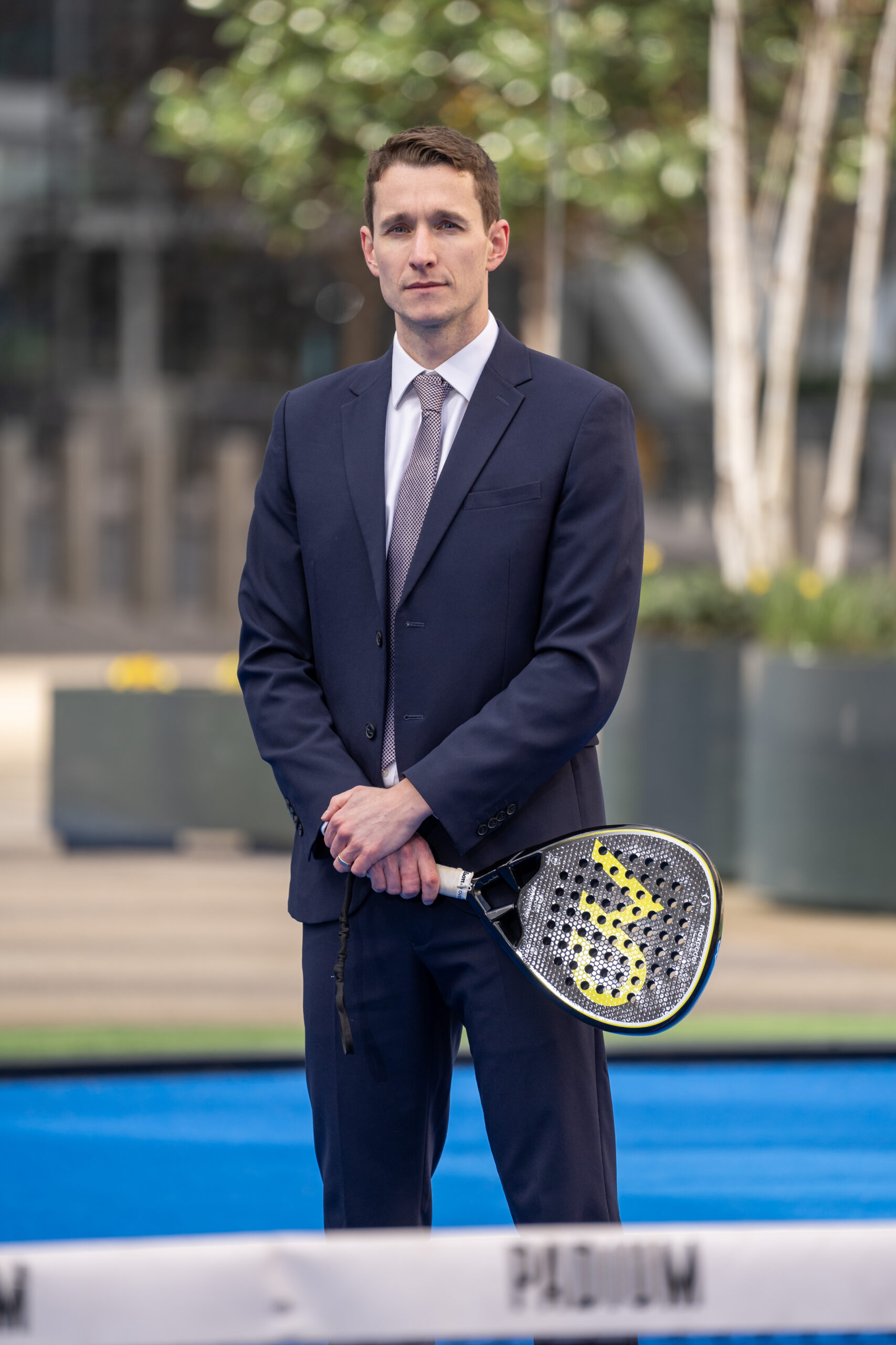Max England standing in a padel court in a suit