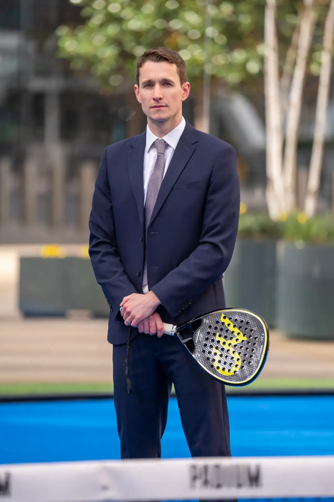 Max England standing in a padel court in a suit