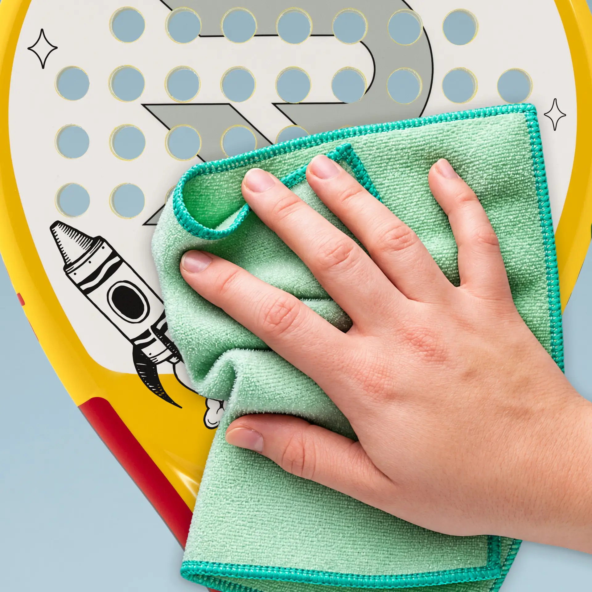 A hand wipes a Raquex x Crayola racket face with a green cloth