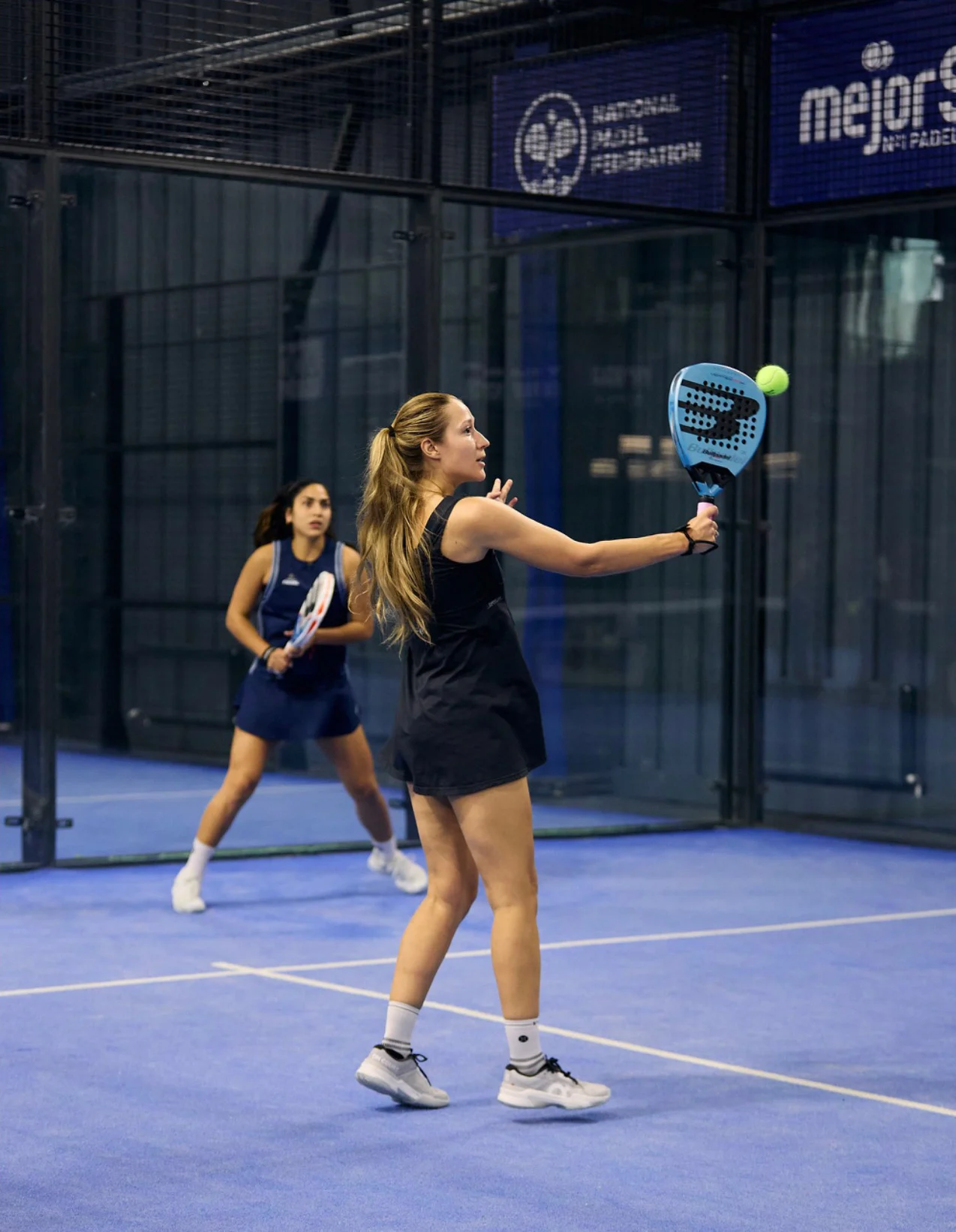 Anna Guryanova hitting a backhand volley in a doubles match on a blue padel court