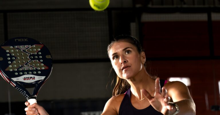 Brittany Dubins tracking the ball as she sets up for an overhead, holding a USPA-branded racket