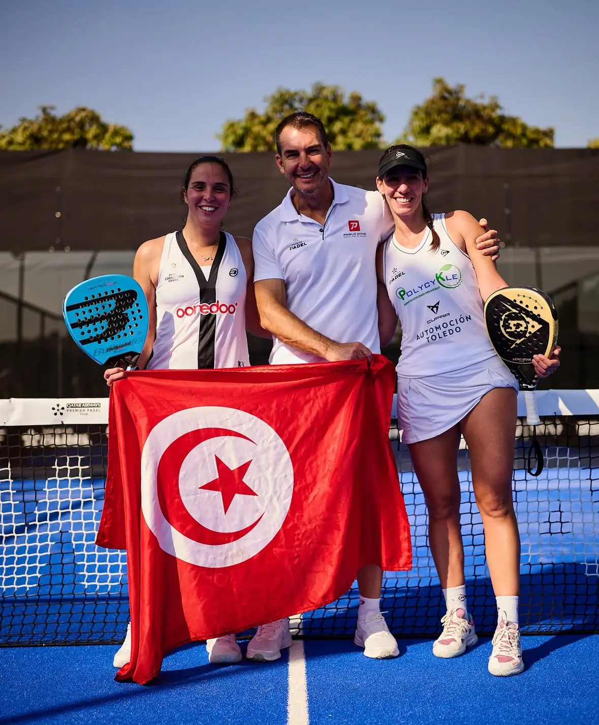 Dora Chamli holding the Tunisian flag on court with her coach and playing partner at a Premier Padel event