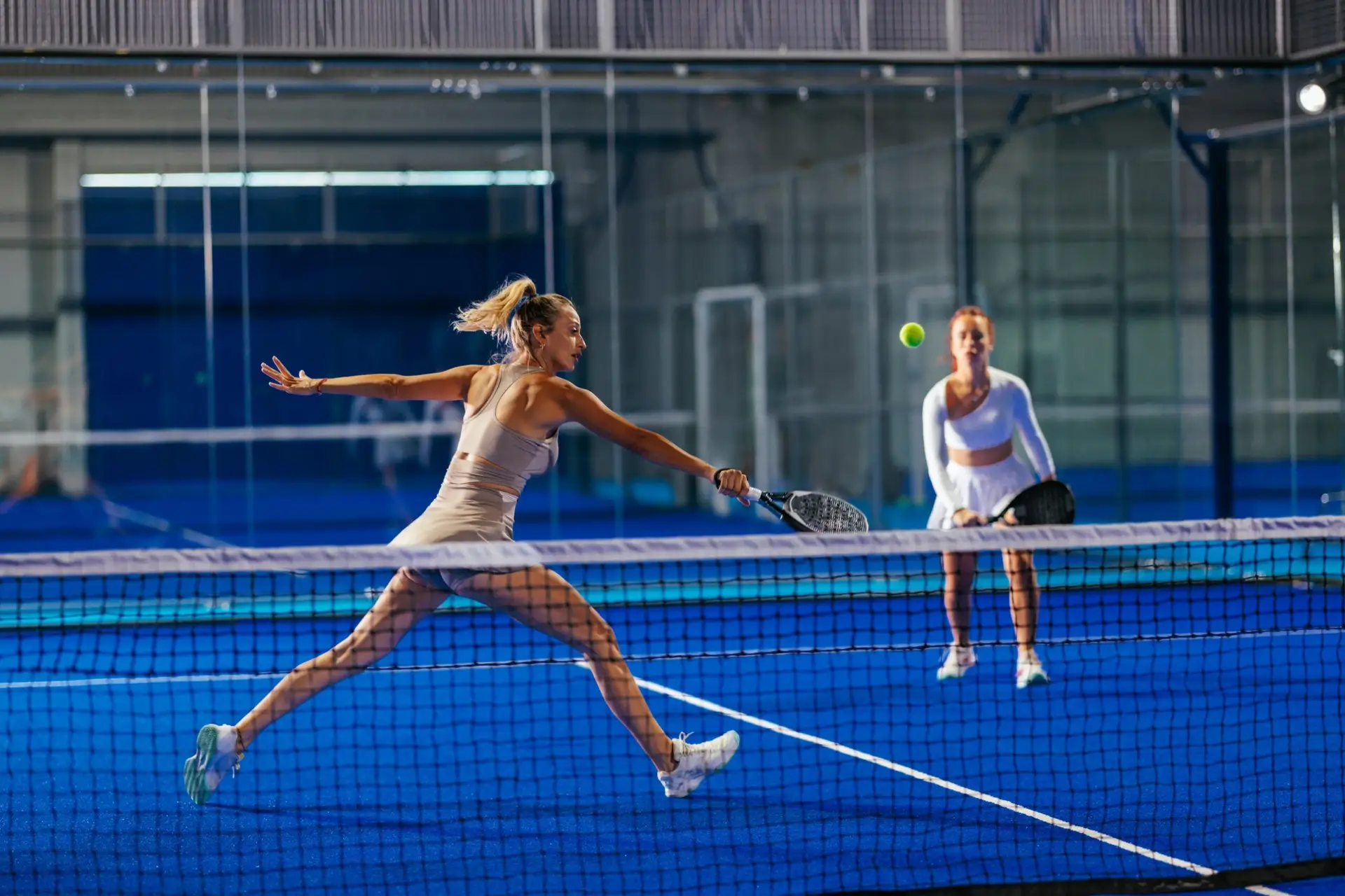 Two padel players at the net during a doubles match on a blue indoor court