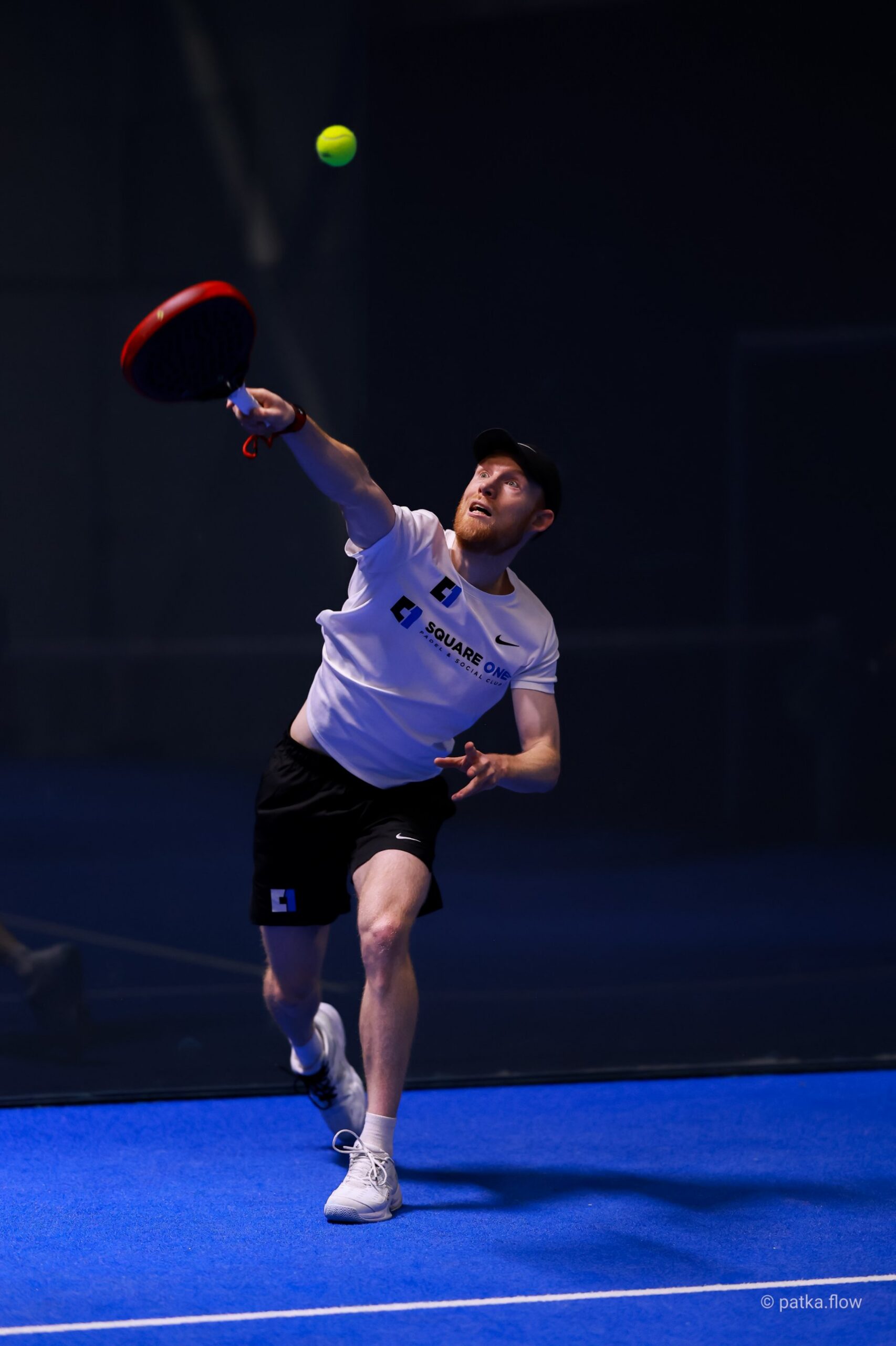 Louis Jarrold reaching high for an overhead on a blue indoor court